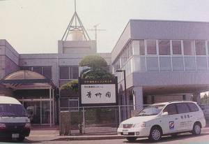 施設の外観。複数階建てのビルと駐車車両が見える街並み
